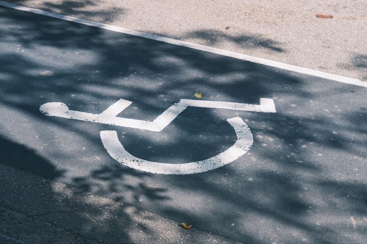 A wheelchair accessibility symbol painted on tarmac, in dappled sunlight through trees