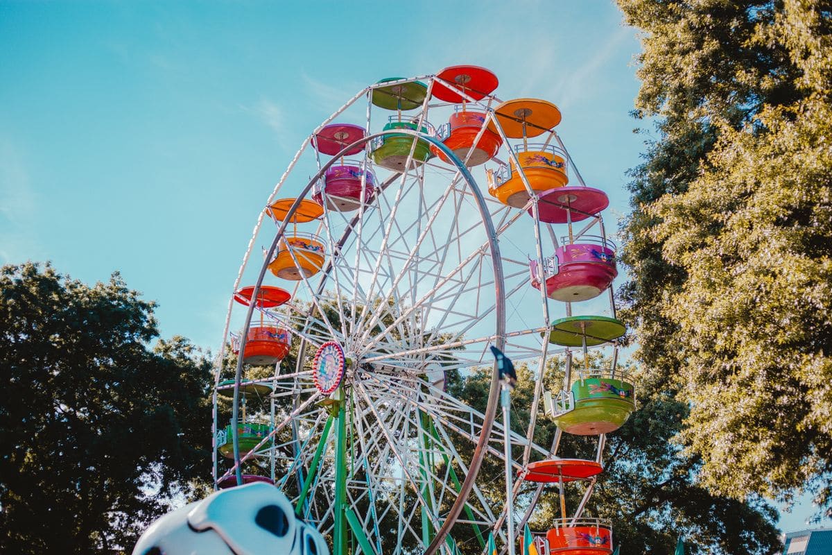 A brightly coloured Ferris wheel at a fairground, set against trees and a blue sky