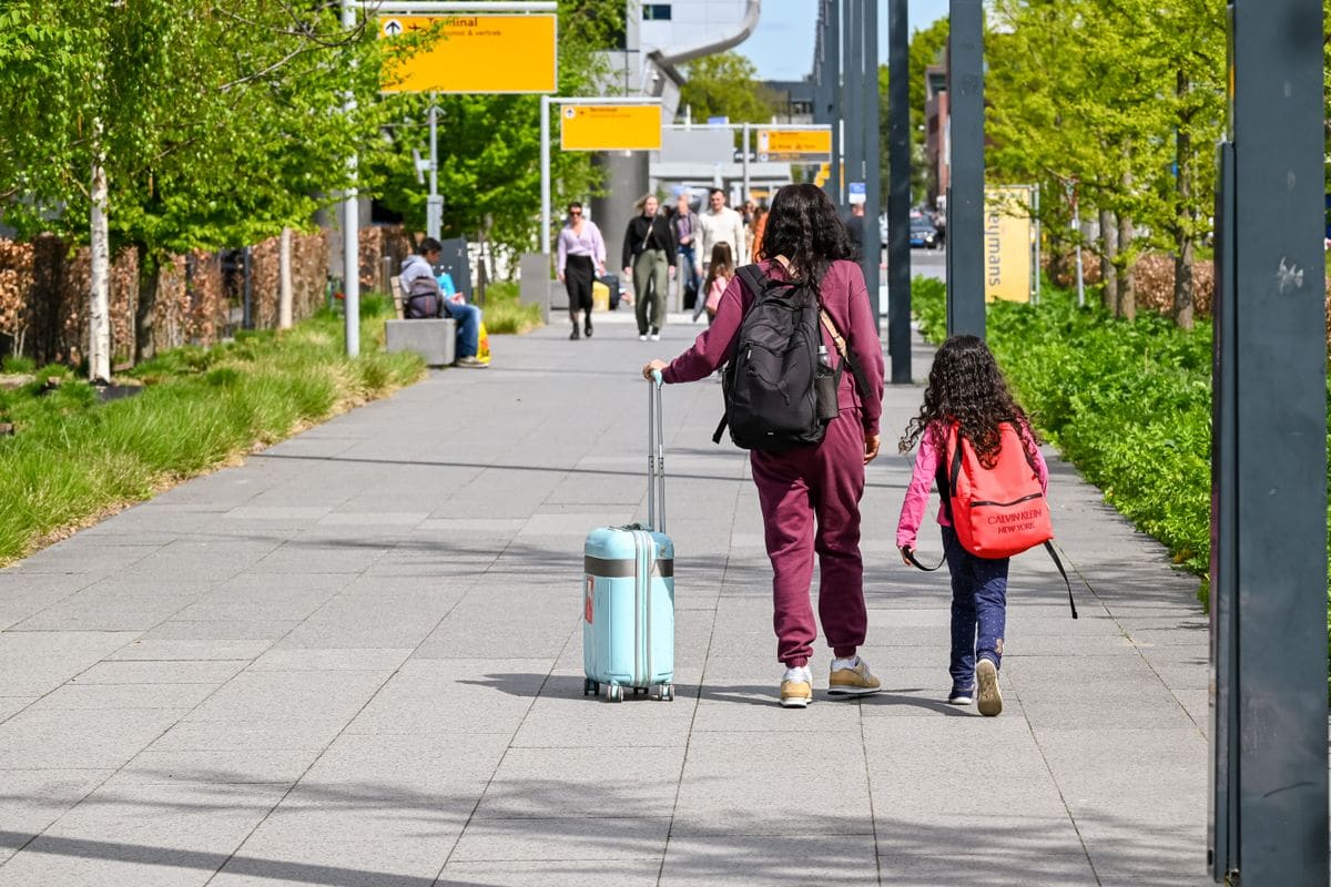 A mother and daughter, seen from behind, walking through an airport concourse pulling suitcases